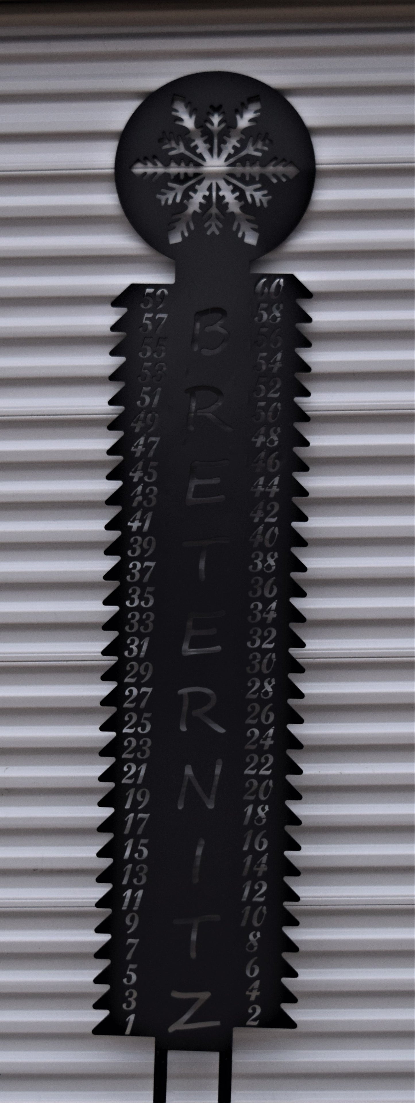 Customizable black metal snow gauge 91 inches tall by 16.5 inches wide. This snow gauge features a snowflake at the top with numbers running up each side. With the customizable last name Breternitz going up the center