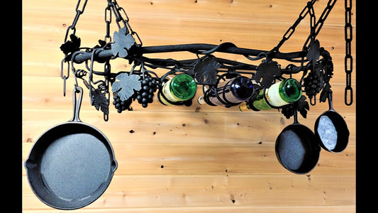 Custom black metal grape theme pot rack with wine holder in center. Holds three wine bottles, and six cast iron pots and pans. Featuring grapes, leaves, and vines. 
