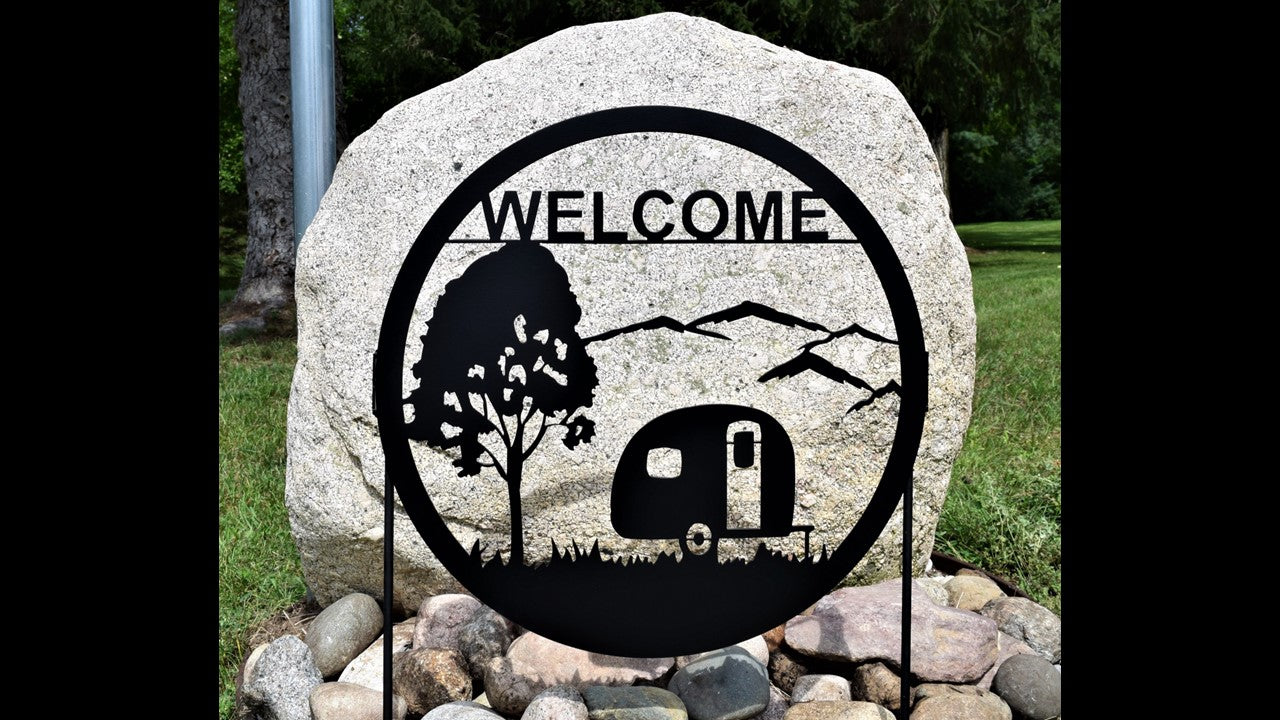 black metal custom welcome silhouette featuring camper with tree, grass and mountains. Sign stakes included. 16 inches by 16 inches. Priced at 60 dollars  SKU number YCW16