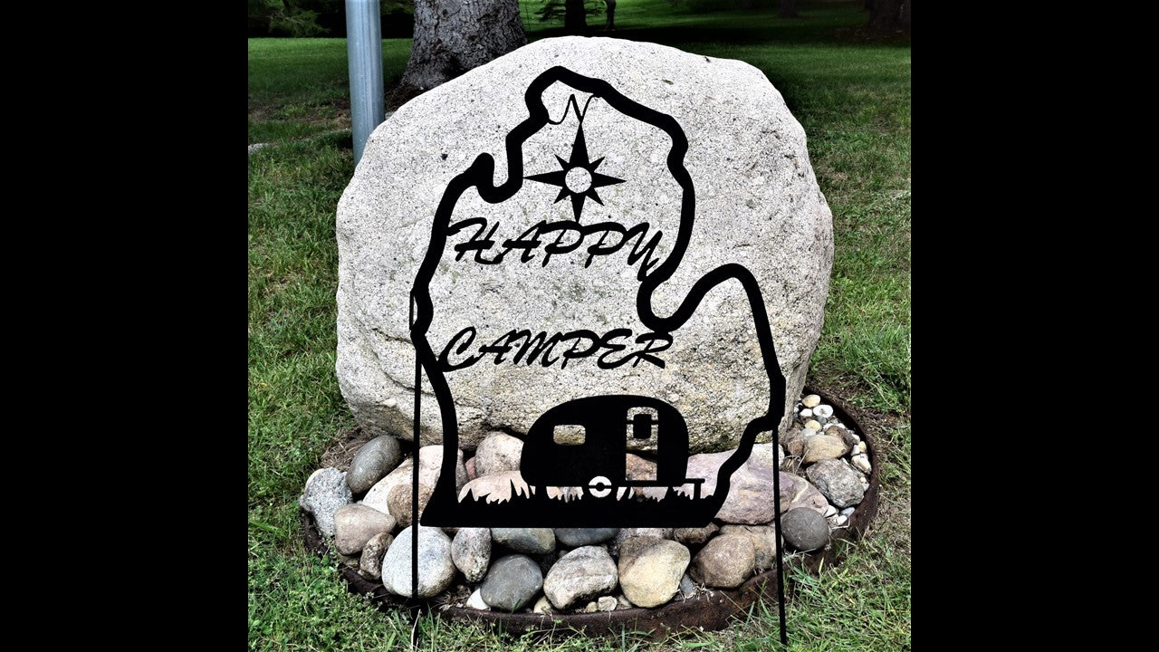 black metal custom yard silhouette of lower Michigan featuring happy camper with camper parked on grass and compass above. Sign stakes are included priced at 80 dollars. SKU number YHCM