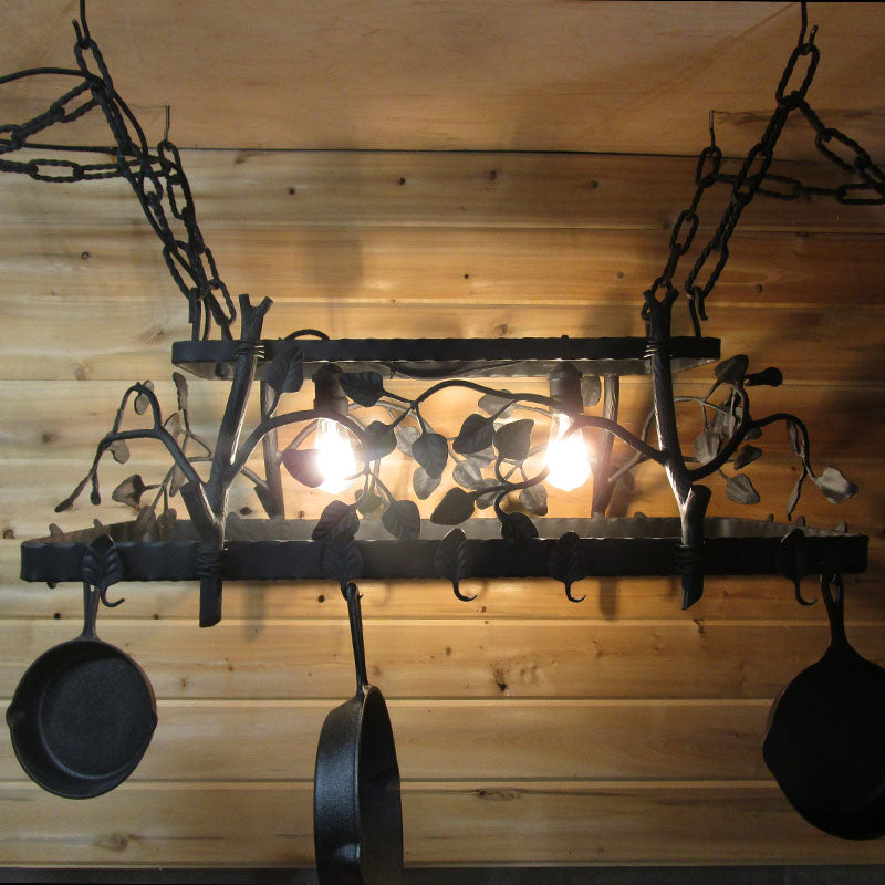Black metal decorative hanging pot rack with dimensional branches, vines, leaf designs and lights set in the middle of the rack.